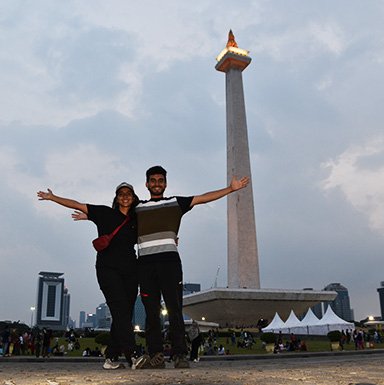 Pareja posando en plaza de Yakarta con torre monumental de fondo.