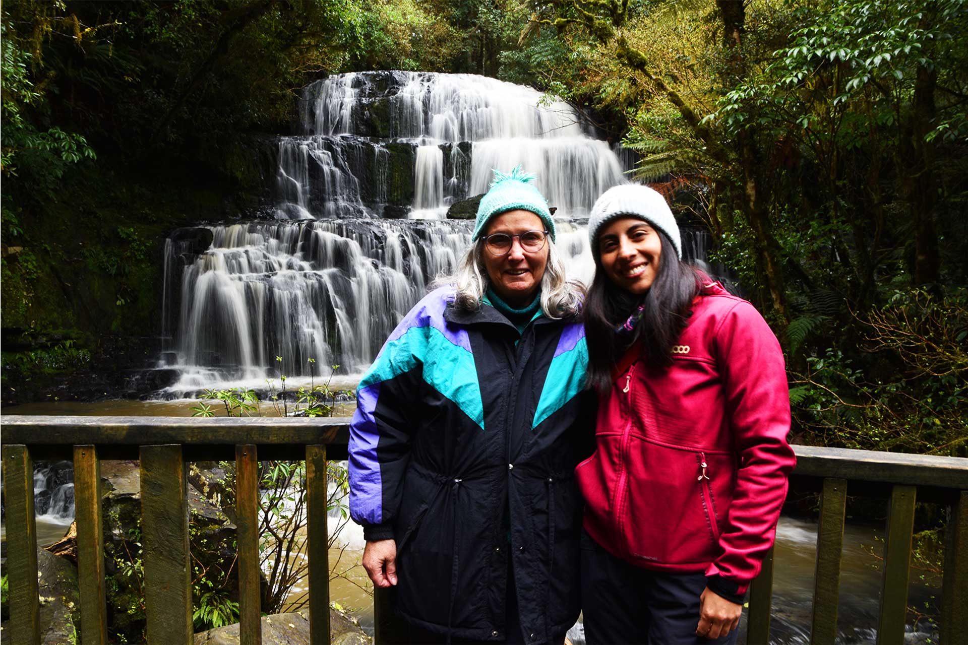 Dos mujeres sonrientes frente a una cascada natural.