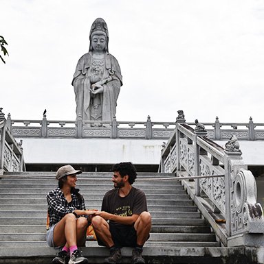 Pareja sentada con Buda de la Misericordia gigante al fondo.